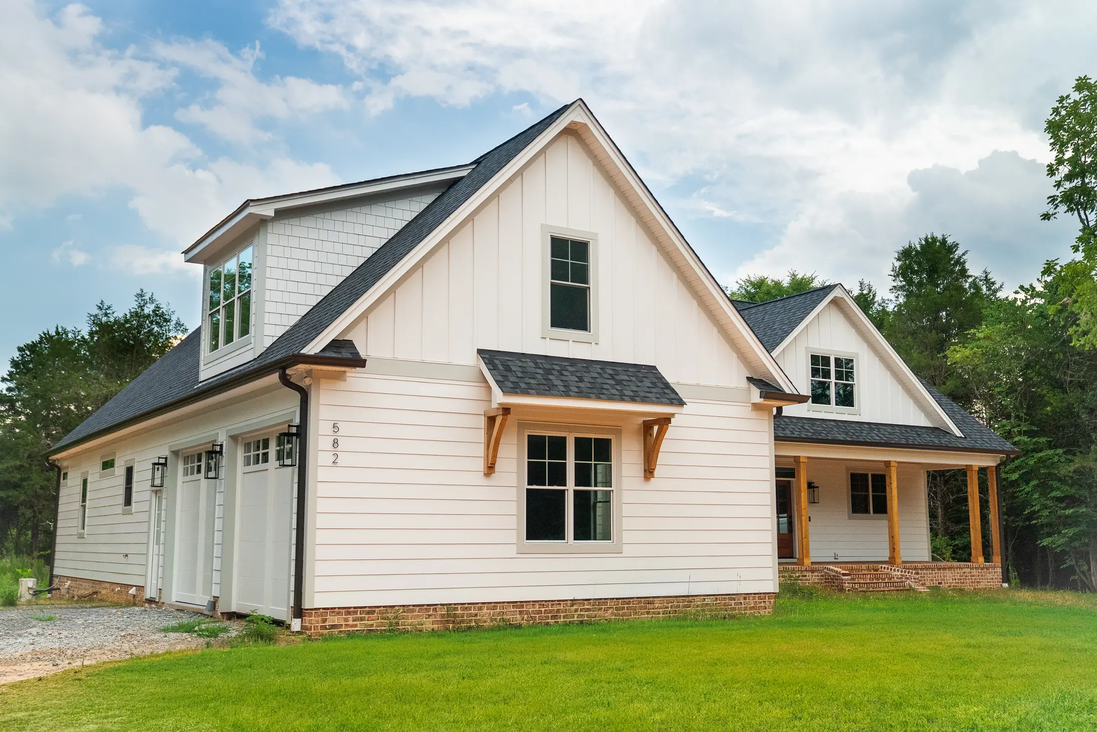 Completed custom home with white board-and-batten siding, cedar brackets and a covered front porch