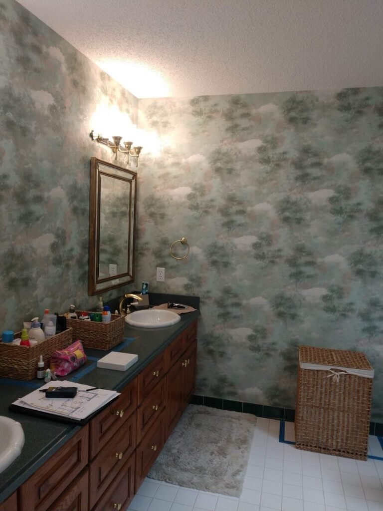 Outdated double vanity with wallpaper and wicker hamper before soaker tub remodel