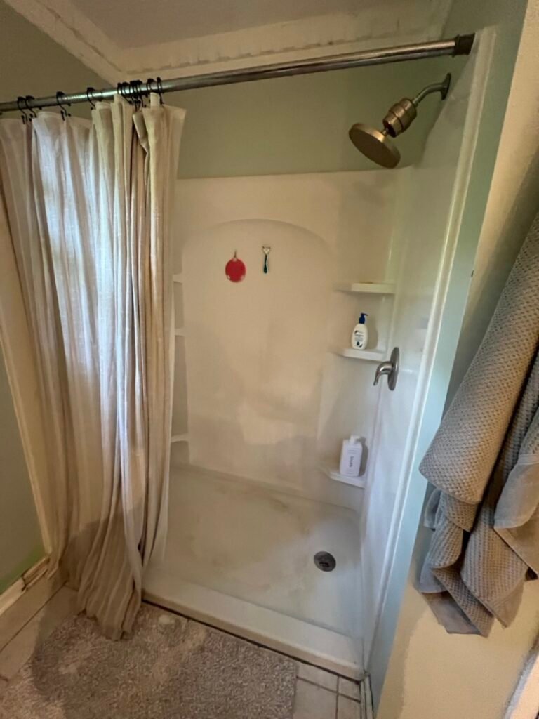 Worn fiberglass shower stall with shower curtain before Grinnell Ct bathroom transformation