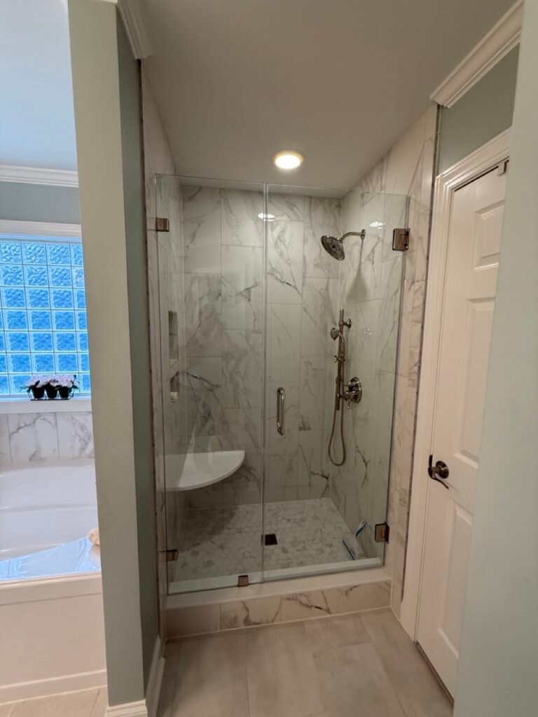 Frameless glass walk-in shower with marble tile and corner bench