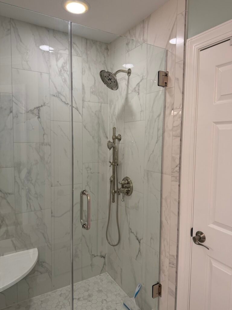 Close-up of brushed nickel rainfall shower head and handheld sprayer on marble wall