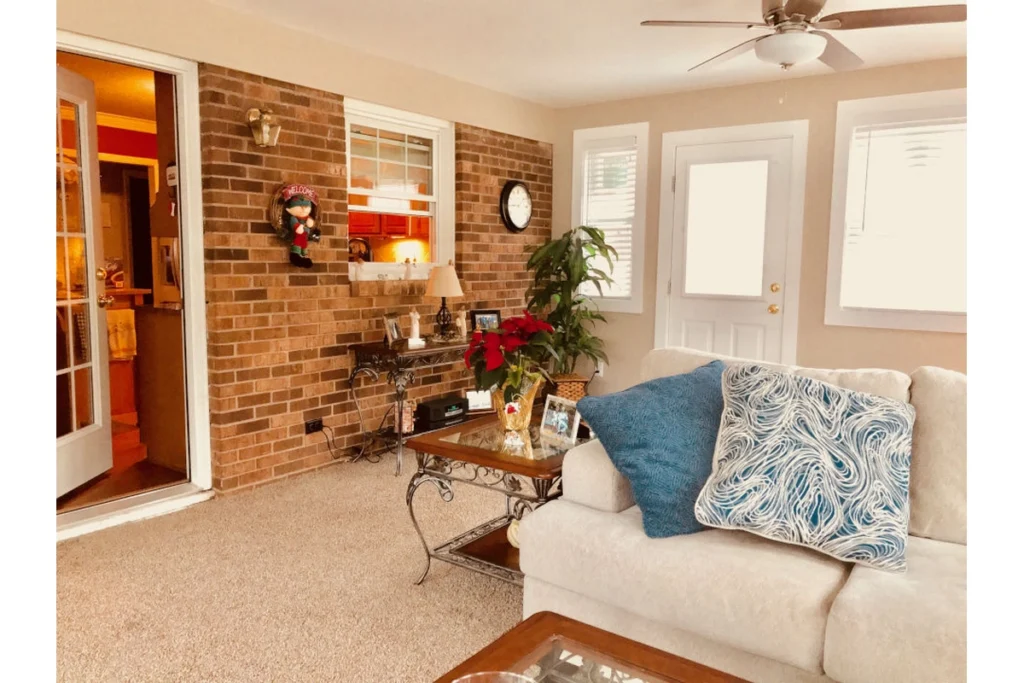 Sunroom addition interior showing brick wall, exterior door, and cozy seating area