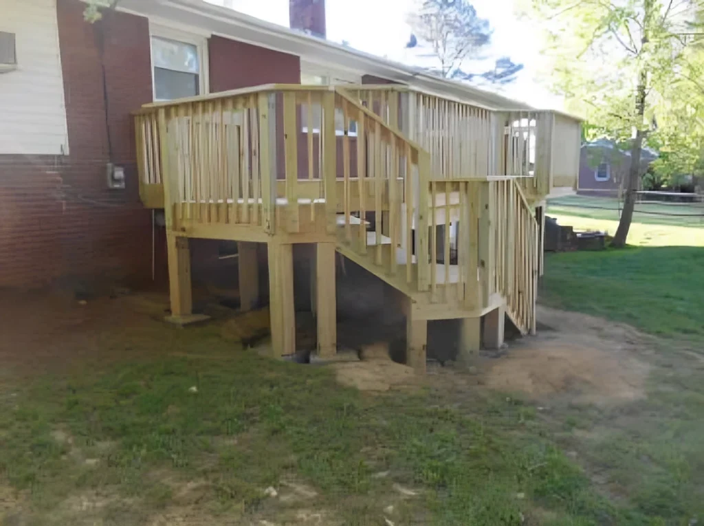 Newly built elevated wood deck with railings and stairs on the rear of a brick home, on posts over a graded yard
