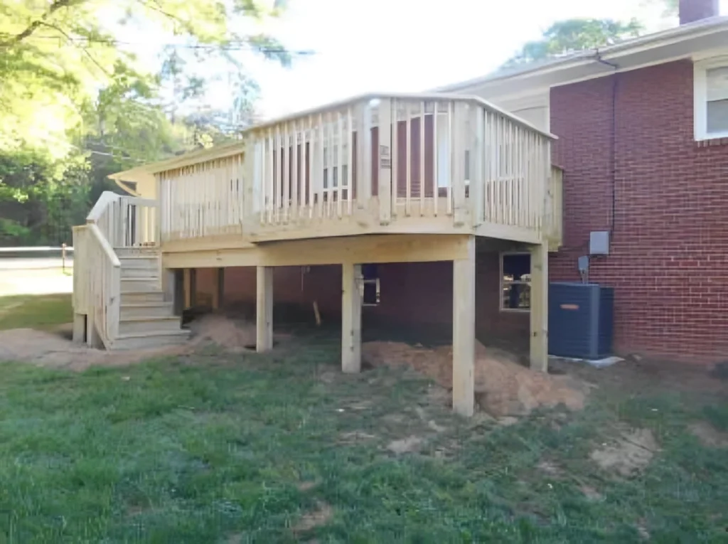 Elevated pressure-treated deck spanning the back of a brick home, with stairs down to the yard beside the AC unit