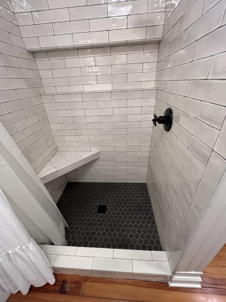 Looking down into the tiled shower at the bench, dark hexagon mosaic floor, square drain and white curb