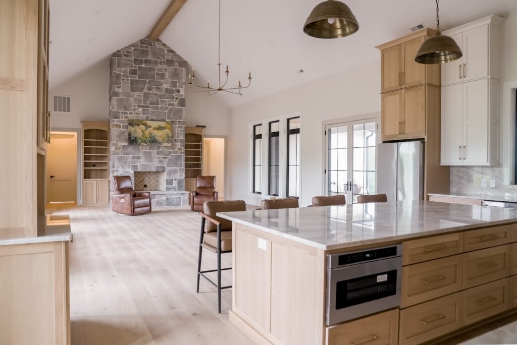 Open great room and kitchen with vaulted ceiling, floor-to-ceiling stone fireplace and marble-topped island