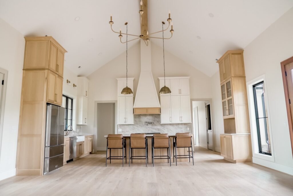 White oak kitchen with plaster range hood, marble backsplash and brass pendant lights under a vaulted ceiling