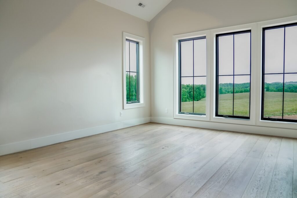 Bedroom with wide-plank white oak floors and black-framed windows overlooking open pasture