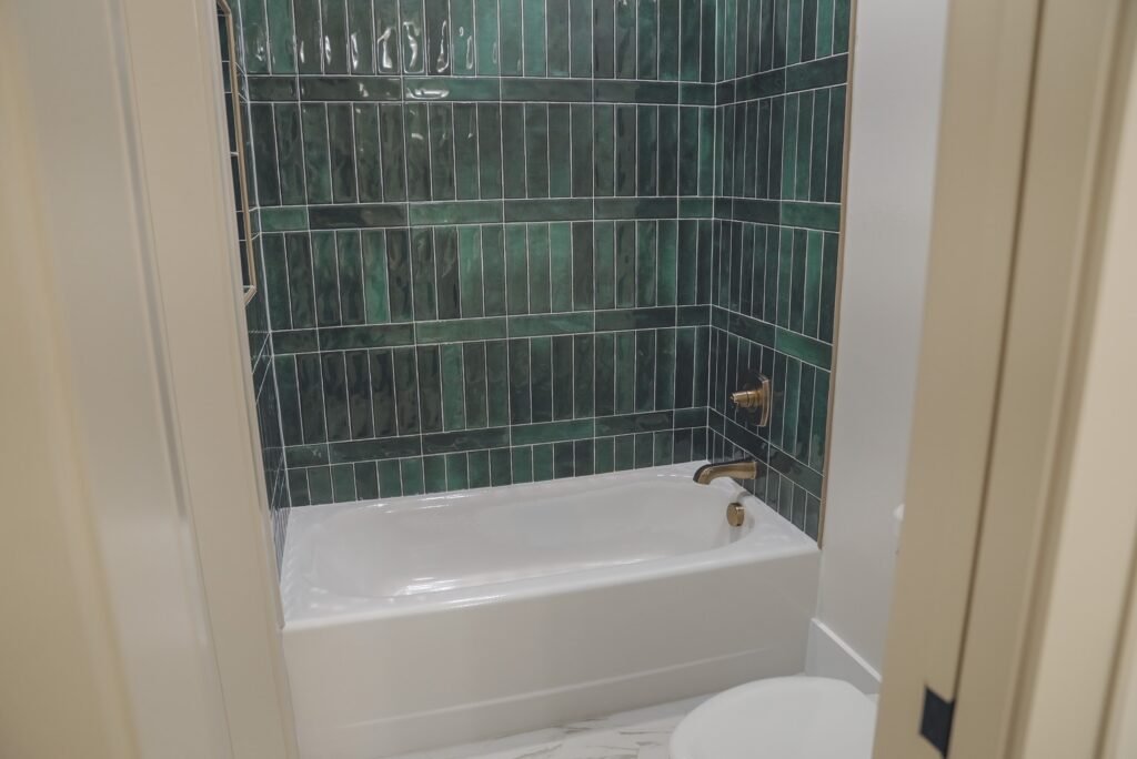 Bathroom with stacked green tile tub surround and brushed brass fixtures