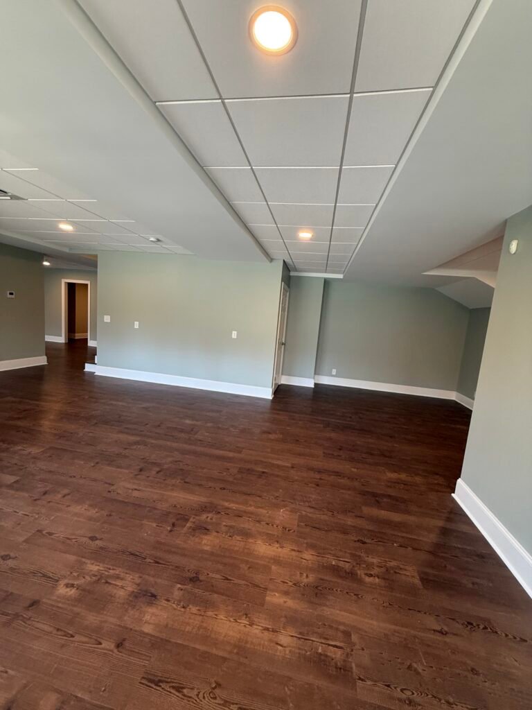 Empty basement living area with sage green walls, white suspended ceiling tiles, recessed lighting and dark wide-plank flooring