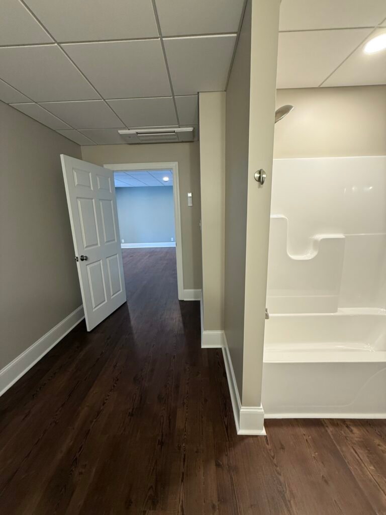 Basement hallway leading to a blue-walled room, with a white tub and shower surround and brushed nickel showerhead