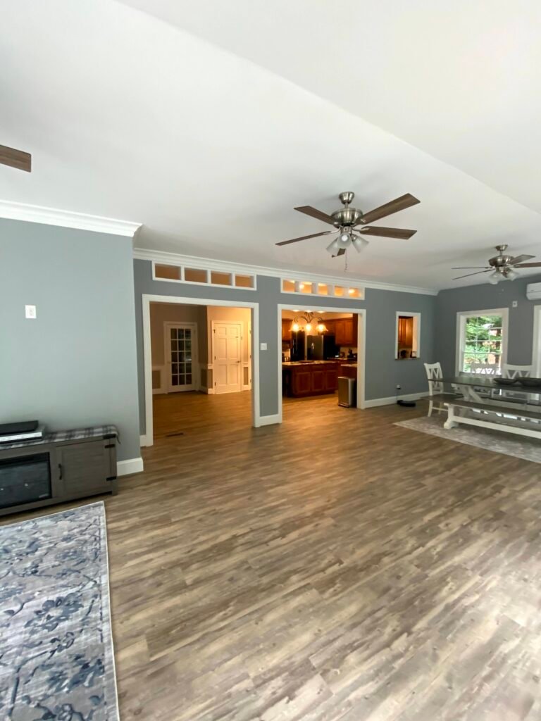 Vaulted white ceiling over grey-blue walls, transom-topped openings framing views to a wood-cabinet kitchen and hallway beyond