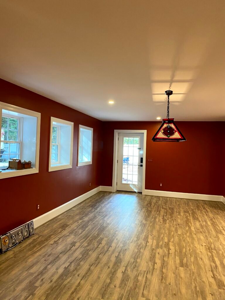 Deep red walls and white trim in an empty room with stained-glass pendant light and plank floor