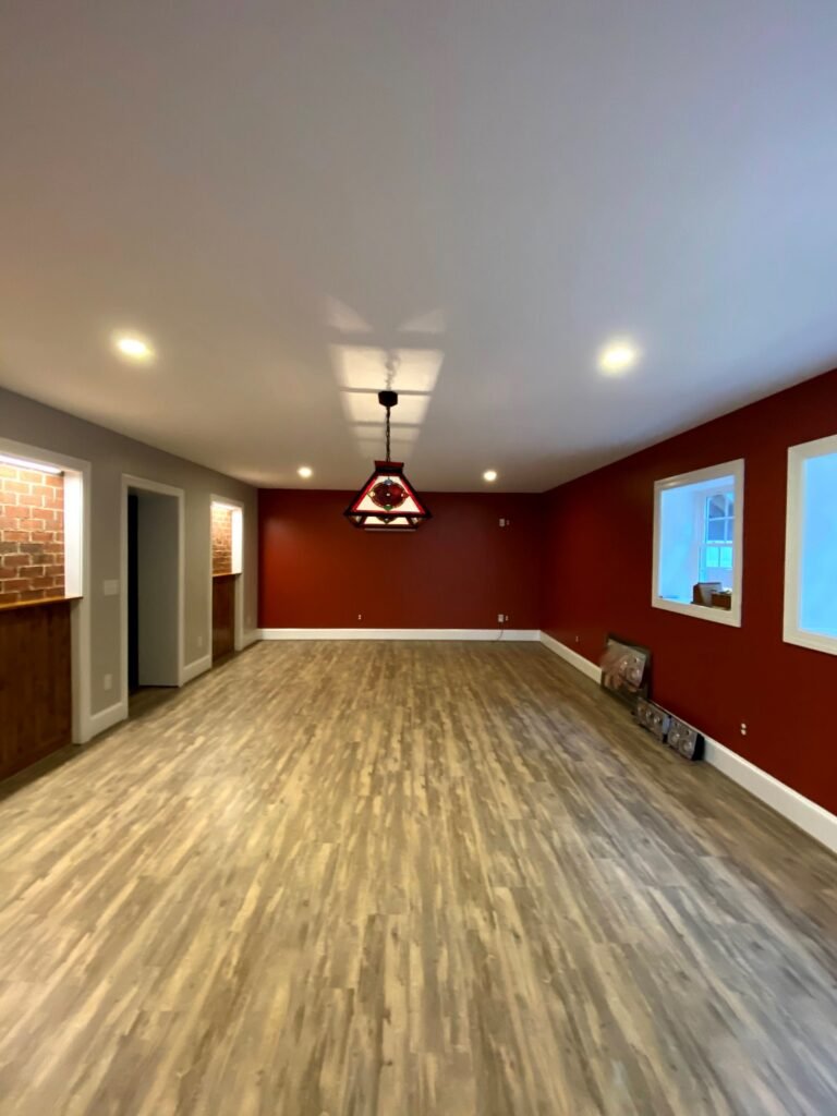 Room with burgundy and grey walls, exposed brick pass-through niches, recessed lighting and wood-look plank flooring