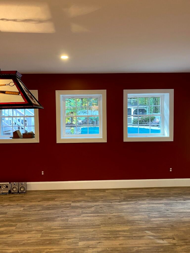 Two white-trimmed windows in a deep red wall overlooking a covered pool and deck, with stained-glass pendant nearby