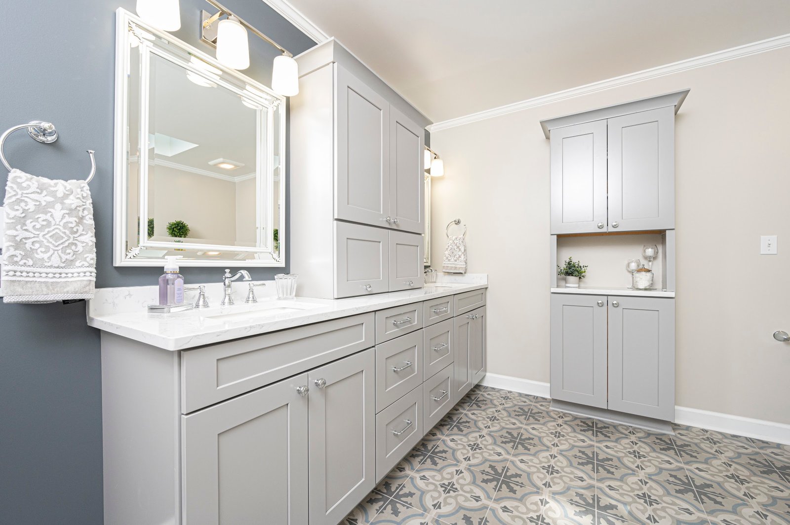 Angled view along grey cabinetry, quartz counter, framed mirror and sconces against a charcoal wall, matching linen tower
