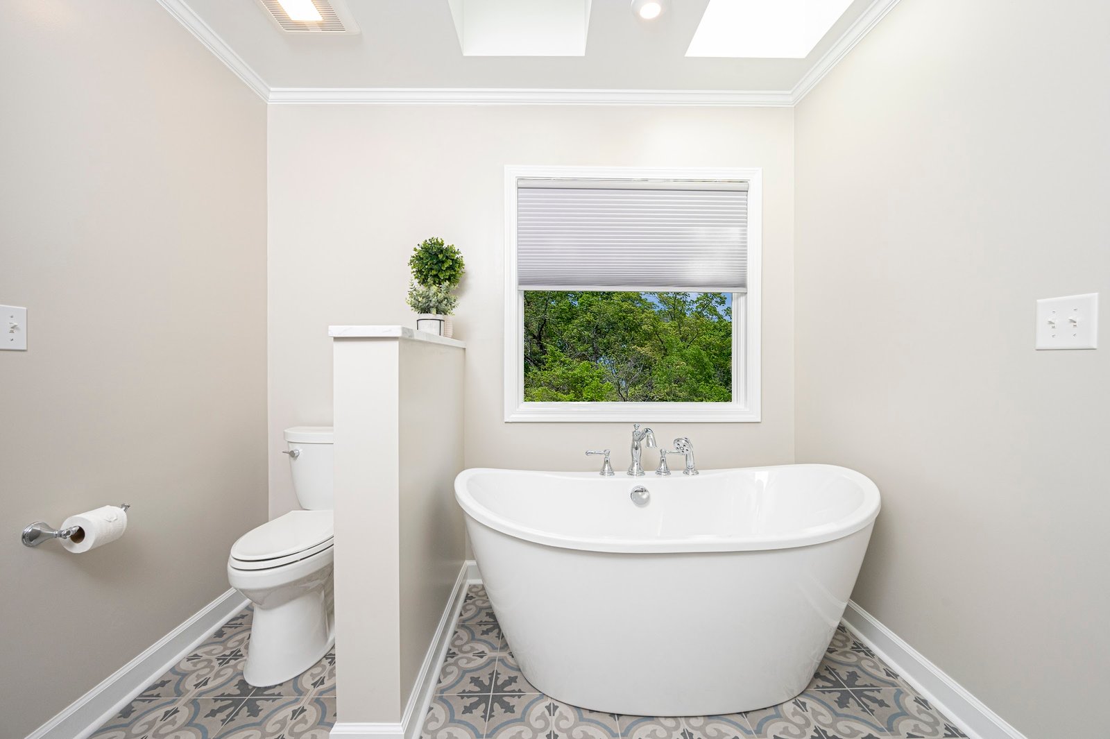 Symmetrical view of the tub centered beneath the window, toilet screened by a low privacy wall, patterned floor tile