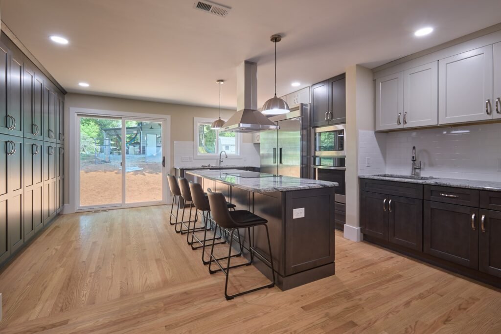 Wide kitchen view with dark shaker pantry wall, sliding glass door, granite-topped island and four black barstools