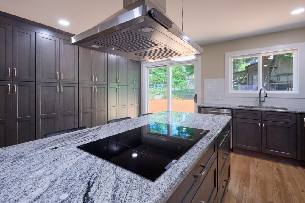 Smooth black cooktop set in speckled grey granite beneath a stainless island hood, tall dark cabinets alongside