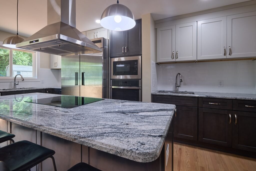 Island granite and cooktop in foreground with white upper cabinets, stainless microwave, wall oven and secondary prep sink