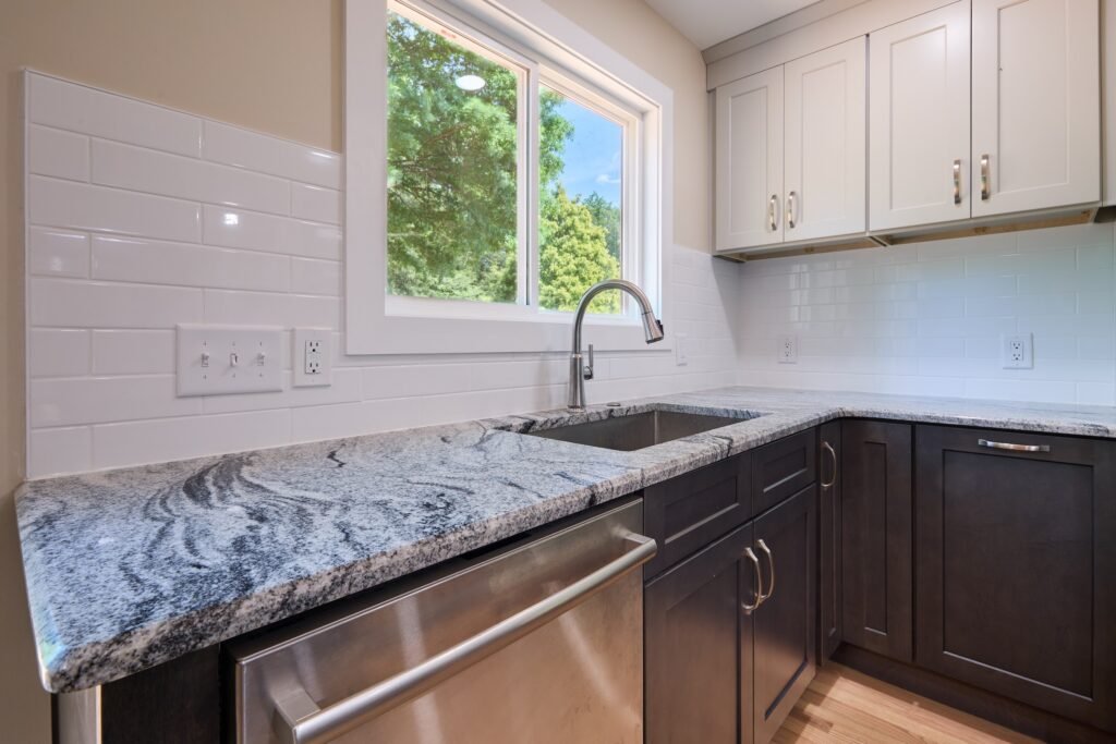 Undermount stainless sink and pull-down faucet below a window, framed by white subway tile and dark base cabinets