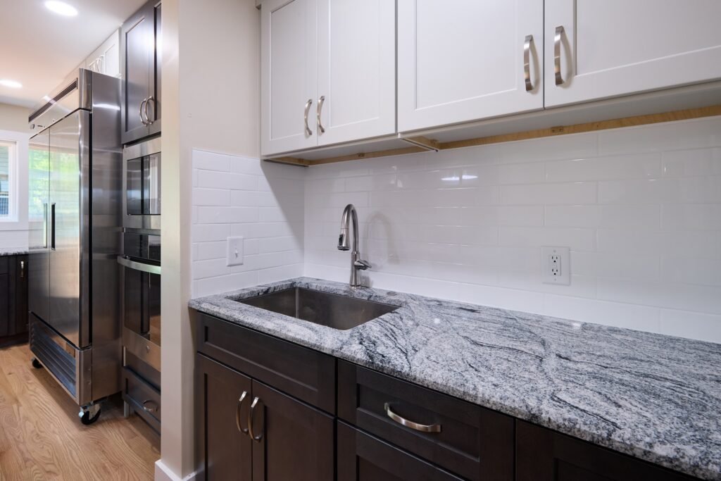 Prep counter with stainless sink and gooseneck faucet, white shaker uppers, subway tile, and granite over dark cabinetry
