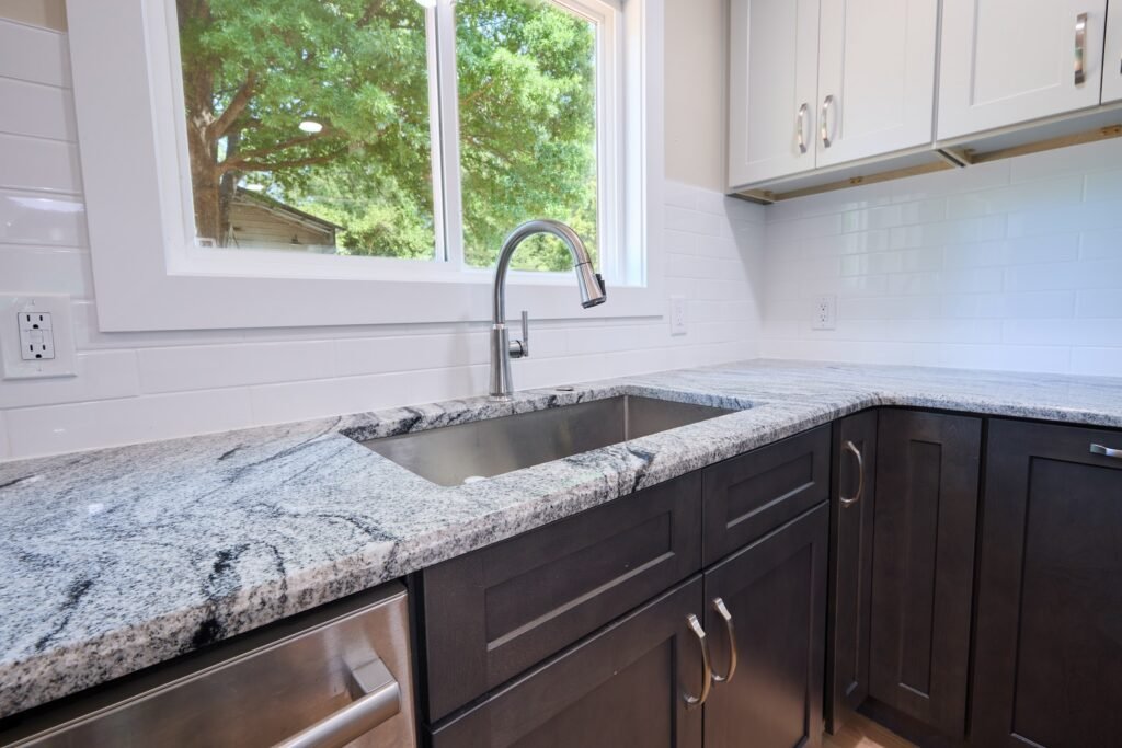 Close view of veined granite countertop wrapping a corner sink, with white shaker uppers and dark base cabinets