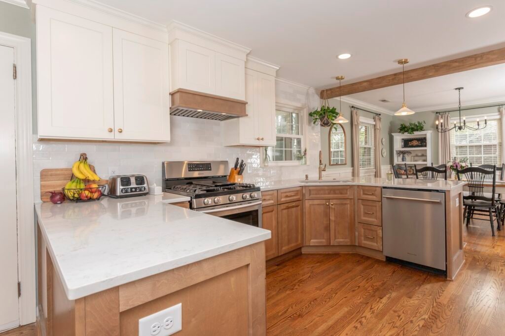 White upper cabinets and stained wood base cabinets meet a white quartz peninsula, stainless range and wood vent hood
