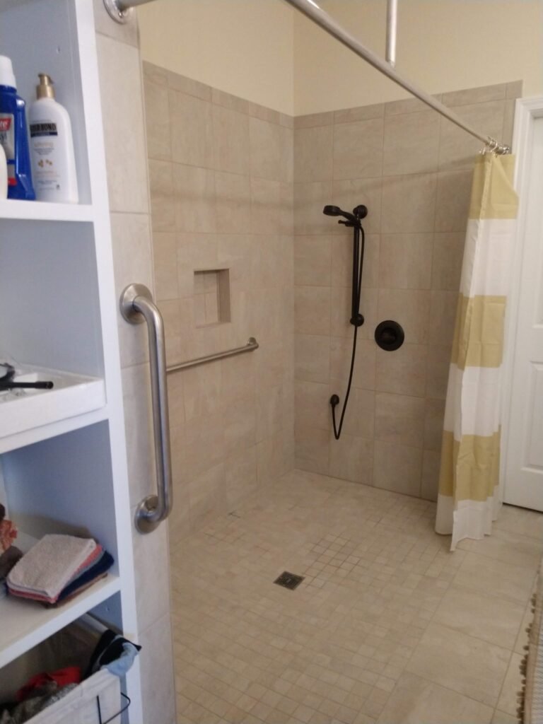 Curbless tiled shower with mosaic floor, handheld sprayer on slide bar, recessed niche, grab bar, and striped curtain