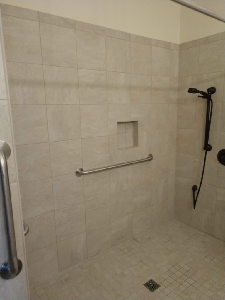 Inside the shower: recessed soap niche, stainless grab bars on two walls, square center drain in mosaic tile