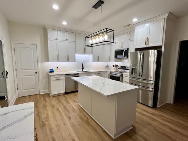 White shaker cabinetry and stainless appliances frame a veined quartz island beneath a linear caged pendant